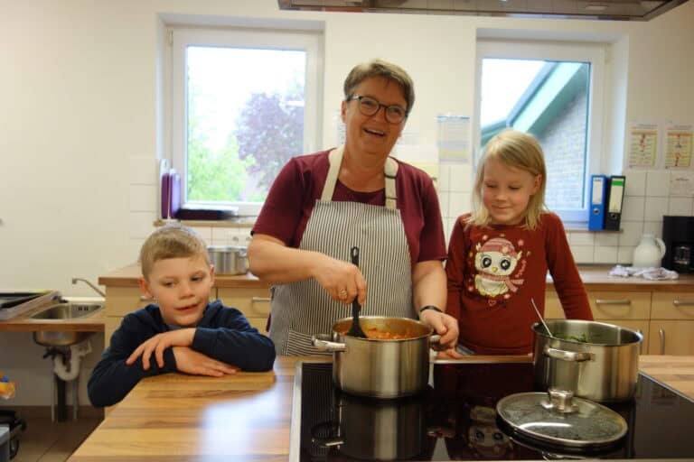 Zwei Kinder mit der Köchin an der Kochinsel beim Kochen